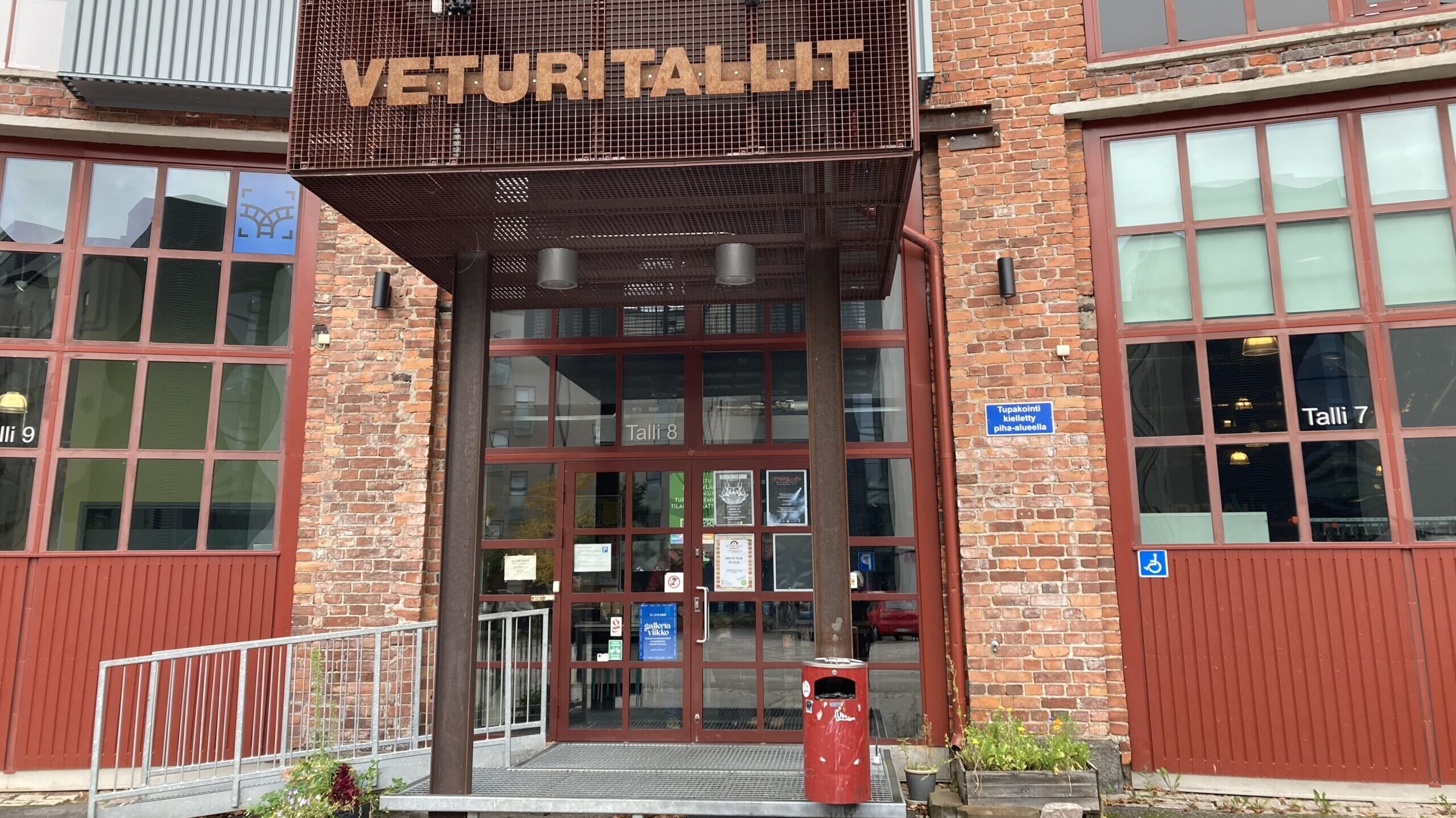 Kuvassa on punatiilisen rakennuksen sisäänkäynti, jonka yllä lukee teksti VETURITALLIT. Sekä ovessa että sen molemmin puolin on paljon lasiruutuja.